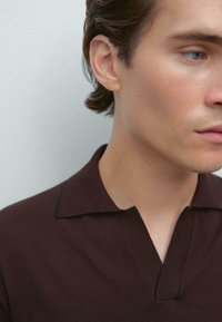 Burgundy polo skjorta med kort krage och V-ringning, med en finstickad struktur och subtila svarta detaljer på kragen.