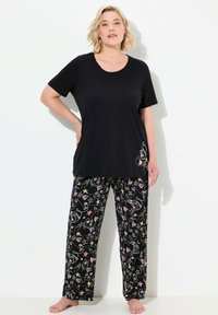 Schwarzes Baumwolloberteil mit kurzen Ärmeln und rundem Ausschnitt, kombiniert mit schwarzen Hosen, die bunte Linienstichmuster von Gesichtern und Sternen aufweisen.