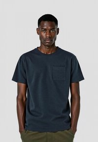 T-shirt in cotone blu navy con scollatura rotonda, maniche corte e taschino frontale. Tessuto liscio, vestibilità comoda, design semplice.