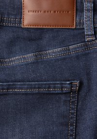 Poche de jean en denim bleu foncé avec étiquette de marque en cuir marron cousue "Street One Studio" au-dessus de la poche.