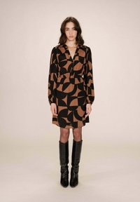 Robe à motifs marron et noir avec un décolleté en V, des manches longues et une taille cintrée, associée à des bottes noires montantes.