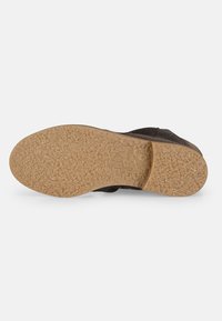 Suela negra de zapato con superficie texturizada, con una suela de goma ranurada de color marrón claro para mayor tracción. Logo de la marca grabado en la suela.