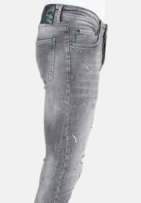 Grijze denim jeans met een fitted ontwerp, voorzien van beschadigde details en een gestructureerde afwerking. De achterpatch bevat een logo.