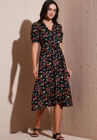 Abito floreale nero con maniche a puff corte, vita con cintura annodata e orlo fino al ginocchio. Presenta motivi floreali colorati in tutto l'abito.