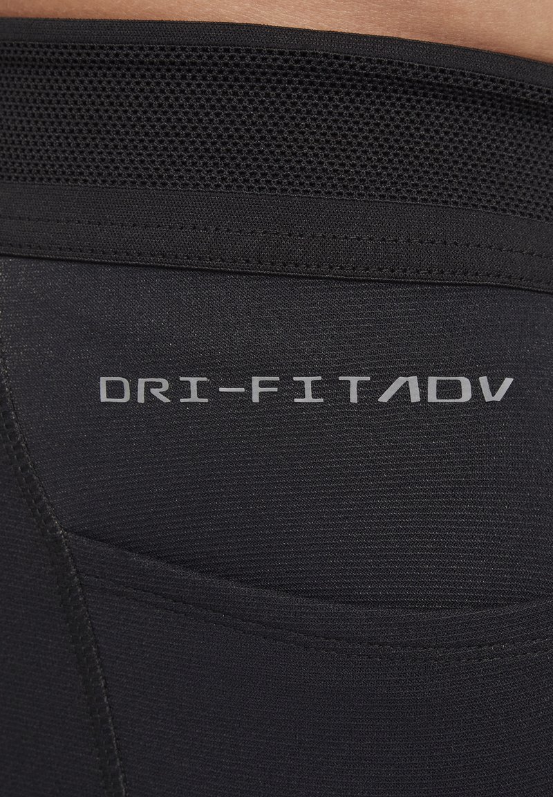 Leggings de sport noirs avec une ceinture en maille texturée, arborant le logo "DRI-FIT ADV" en argent à l'arrière et une finition en tissu lisse.