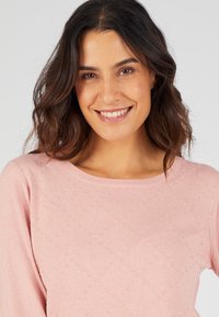 Maglione rosa chiaro a maglia con scollo rotondo e un sottile motivo testurizzato. Maniche lunghe, tessuto morbido e silhouette aderente.