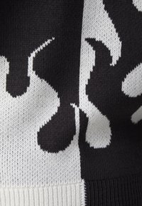 Gebreide trui met een gedurfd zwart-wit patroon en abstracte vormen. Zachte textuur en geribbelde zoomdetail versterken het ontwerp.