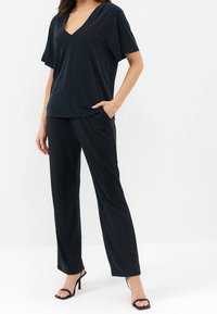 T-shirt nero a v con maniche corte abbinato a pantaloni neri a gamba larga. Entrambi gli articoli hanno una texture morbida e una vestibilità rilassata, con tasche laterali.