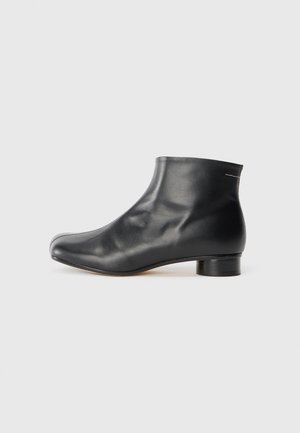 Sorte lærreim ankelstøvel med en glatt finish, rund tå, lav hæl og minimalistisk design. Har diskret søm bak.