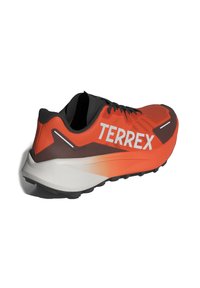 Terrex bėgimo batai oranžinės ir juodos spalvos, su kvėpuojančia viršutine dalimi, tekstūruotu paviršiumi, išsiskiriančiu logotipu ir tvirtu guminio pado sluoksniu.