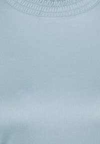 Tessuto a coste di un blu chiaro con una texture liscia, caratterizzato da un collo rotondo e una leggera lucentezza. Visione ravvicinata del design del tessuto.