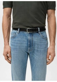 Musta nahkavyö hopeisella soljella, yhdistetty vaaleansinisiin farkkuihin ja tummanvihreään lyhythihaiseen paitaan. Painotus istuvuudessa ja materiaalin tekstuurissa.