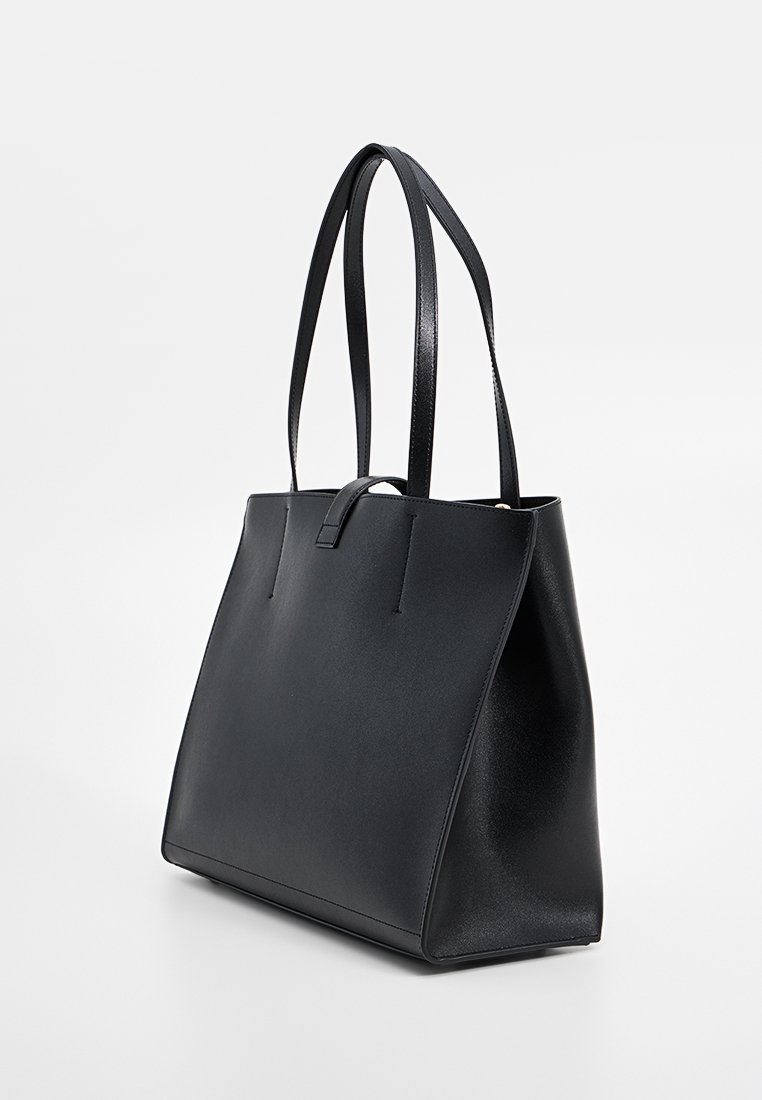 Sac fourre-tout en cuir noir avec doubles poignées plates, texture lisse, design minimaliste et ouverture sur le haut. Présente une forme structurée et aucun matériel visible.