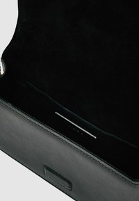 Fekete bőr kézitáska puha velúr belső térrel. Tartalmaz egy kicsi zsebet és rendezett varrást a széleken. Minimál stílusú design.