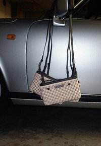 Twee kleine, beige handtassen met een gestructureerd oppervlak en zwarte accenten hangen aan een autospiegel. De tassen hebben ritsen en schouderbanden.