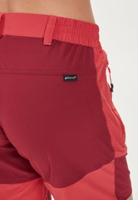 Röda och rosa idrottsshorts med en flexibel midja, sidoficka och en logomärkning. Tyget ser slätt ut, med kontrasterande färgblockering.