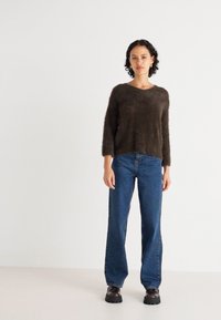 Brauner, flauschiger Pullover mit langen Ärmeln, kombiniert mit blauen weiten Jeans und schwarzen klobigen Schuhen. Einfaches Design, weiche Textur und lässige Passform.