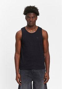 Black sleeveless tank top made of textured fabric, featuring a round neck and small logo on the chest, paired with gray shorts.