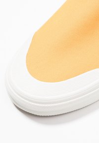 Gelber Leinensneaker mit weißer Gummisohle, strukturierter Oberfläche und abgerundetem Zehendesign mit kontrastierender Farbnuance.