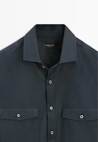 Donkergrijs overhemd met knoopsluiting, gemaakt van gladde stof, met een klassieke kraag en twee borstzakken met zilveren knopen.