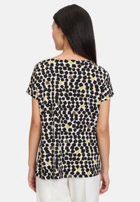 Korte mouwen top van lichtgewicht stof, met een zwart, olijfgroen en geel abstract patroon op een crème achtergrond.