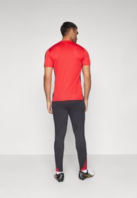 Rød træningsshirt med korte ærmer, kombineret med sorte leggings med røde detaljer ved anklerne. Glat, tætsiddende materiale hele vejen igennem.