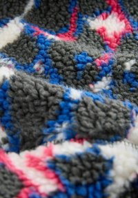 Tissu polaire doux texturé avec des motifs géométriques abstraits gris, bleu, blanc et rose en gros plan.