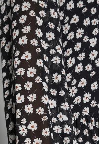 Floraler Stoff für Kleider mit schwarzem Hintergrund, weißen Blumen und braunen Akzenten, zeigt eine leichte, transparente Textur.