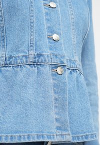 Φωτεινό γαλάζιο τζιν σακάκι με σχέδιο πεπλούμ, ασημί κουμπιά και ορατές ραφές κατά μήκος των ραφών.