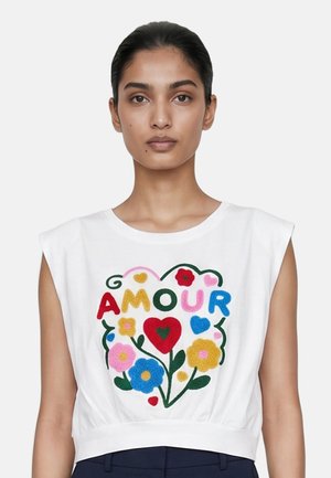 Donna che indossa un top bianco senza maniche con ricamo floreale colorato e la parola "AMOUR" mostrata in rosso, giallo, rosa, blu e verde.