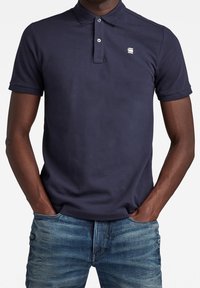 Námořnická modrá polo tričko vyrobené z bavlněné tkaniny se slim fit střihem, s tříknoflíkovou légu a malým logem na levé hrudi.