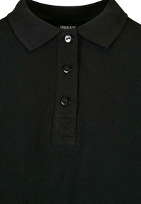 Svarte polo-skjorte med ribbet krage, tre svarte knapper og tekstil med struktur. Har en logomerke inni kragen.