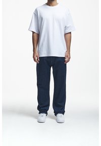 Camiseta blanca de algodón con un corte relajado, combinada con jeans de mezclilla azul oscuro y zapatillas blancas. Conjunto sencillo y casual para el día a día.