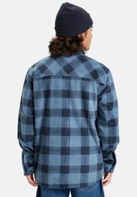 Camisa de franela a cuadros en azul y marino con mangas largas, cierre de botones y una textura suave. Presenta un cuello estándar y un dobladillo curvado.