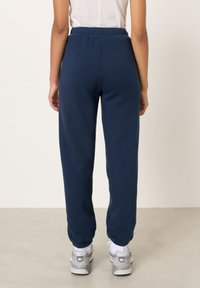 Tmavomodré teplákové nohavice s elastickým pásom, zužovanými nohavicami a rebrovanými manžetami, vyrobené z mäkkého materiálu. Kombinované so sivými športovými topánkami.