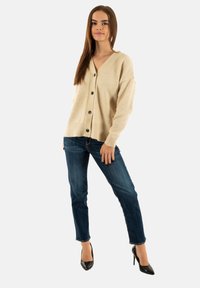 Cardigan beige con scollatura a V, chiusura con bottoni e orlo a coste. Abbinato a jeans blu e décolleté nere a punta. Tessuto morbido e vestibilità comoda.