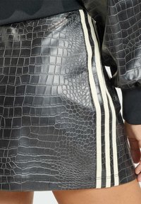 Černá mini sukně z umělé kůže s krokodýlím vzorem, zdobená dvěma bílými svislými pruhy po straně. Hladký, lesklý povrch.