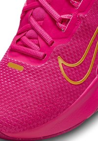 Zapatilla deportiva de color rosa brillante con empeine de malla texturizada, logo de swish dorado y cordones planos. Punta redondeada y suela acolchada para mayor soporte.