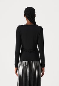 Top nero a maniche lunghe con una texture liscia, caratterizzato da un design aderente e un accento drappeggiato sul retro, abbinato a una gonna plissettata in argento metallico.