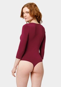 Body mauve à manches longues avec un col rond, coupe ajustée, et une taille haute qui accentue le dos. Texture douce.
