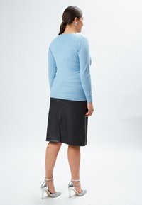 Helles blaues Langarmoberteil mit geripptem Saum, kombiniert mit einem schwarzen Lederrock. Schuhwerk: silberne Glitzerabsätze. Einfaches Design, glatte Textur.