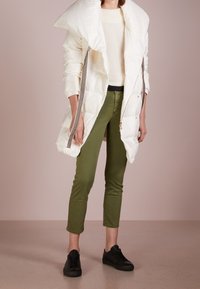 Vit puffjacka med överdimensionerad krage, dragkedjesidor och en texturerad finish, kombinerad med olivgröna byxor och svarta sneakers.