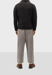 Maglione scuro con texture e colletto a scialle, abbinato a pantaloni in velluto a coste grigi chiari e scarpe in suede marroni, viste da dietro.