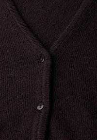 Mörkbrun kofta med en texturerad stickad mönster, V-ringning och tre svarta knappar fram. Mjuk material med ribbade kanter.