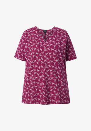 Lyhythihainen magentanvärinen pusero, jossa valkoiset abstraktit raapustukset ja pyöreä pääntie, esitetty valkoista taustaa vasten.