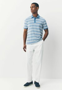 Lühikeste varrukatega polo-särk, millel on sinised ja valged horisontaalsed triibud, nööbitav krae, kantud valgete pükste ja tumesiniste vabaajajalatsitega.