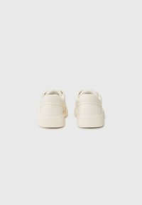 Baskets blanches avec une tige en cuir lisse, un col rembourré et un design bas. Semelle en caoutchouc texturée et style minimaliste.