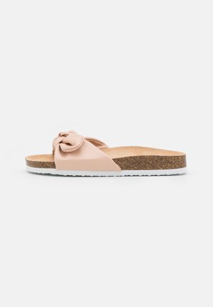 Sandale mule nude avec une tige en cuir nouée, une semelle intermédiaire en liège et une semelle extérieure en caoutchouc blanc. Texture lisse et design minimaliste.