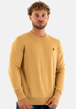 Maglione a maglia color oro con maniche lunghe, scollatura rotonda e polsini a coste. Presenta un piccolo logo nero sul petto.