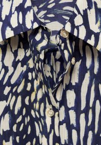 Gros plan sur une chemise en velours côtelé à motifs bleus et blancs, avec des boutons en perles et un col pointu.